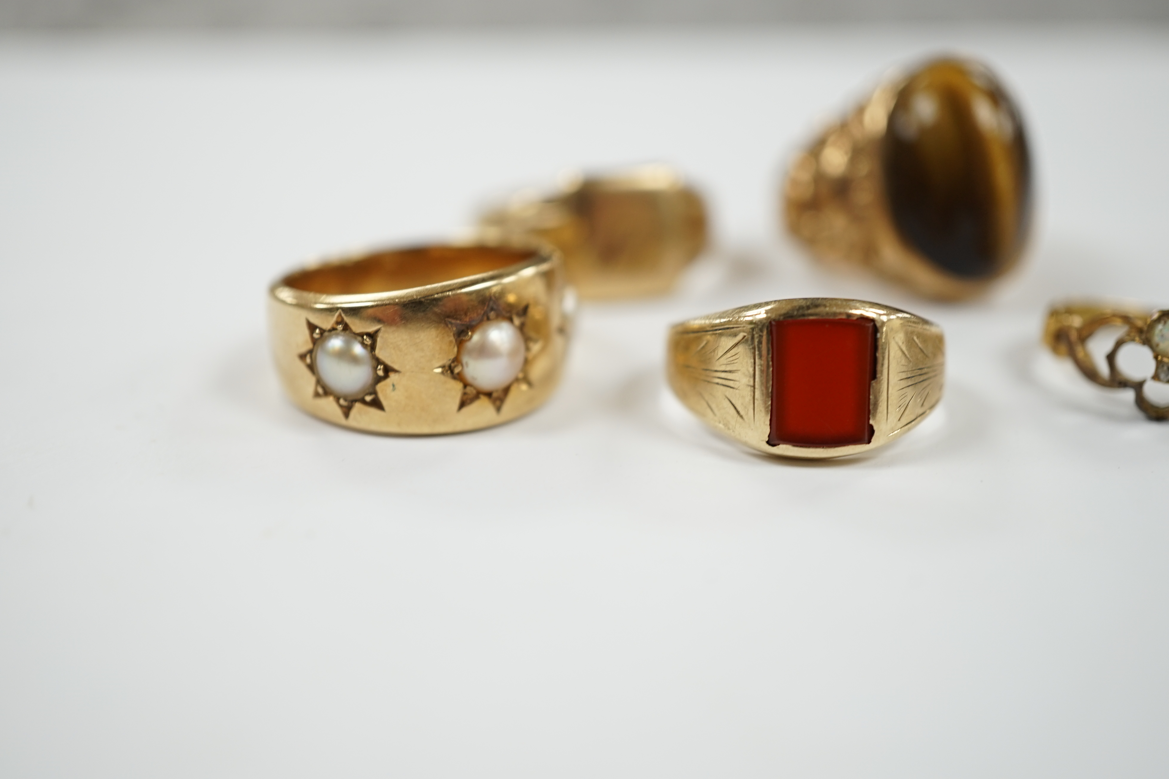A 9ct gold signet ring, a gold and carnelian set signet ring and three yellow metal rings one set with three split pearls and one set with tiger's eye quartz cabochon, gross weight 29.7 grams.